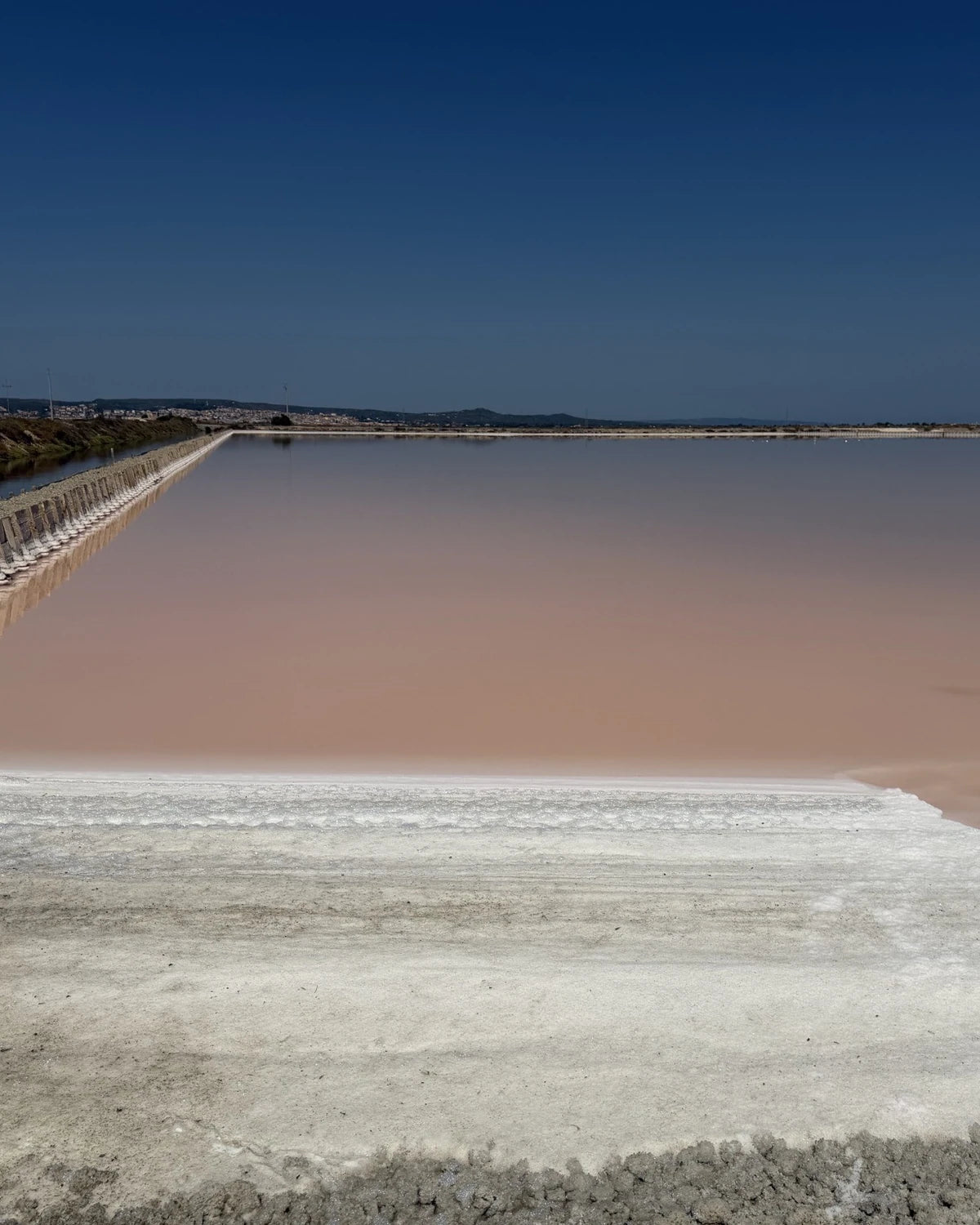 A people-free pink salt pond bordered by pale mineral banks during a visit in Italy